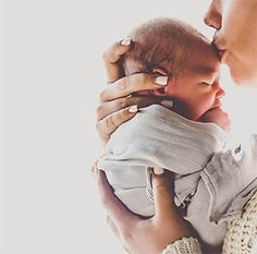 a woman holding a baby in her arms and kissing it's face to the side