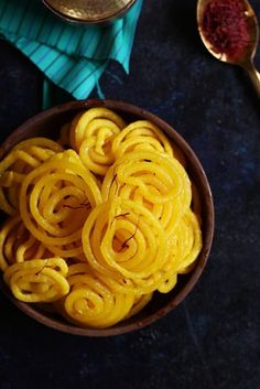 a bowl filled with yellow noodles next to spoons on top of a blue table