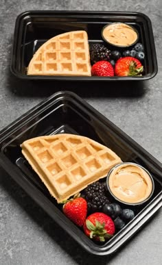 two black trays filled with waffles, berries and peanut butter on top of each other