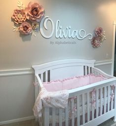 a white crib in front of a wall with pink flowers and name written on it