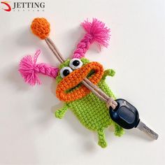 a crocheted frog holding a pair of scissors on top of a white surface