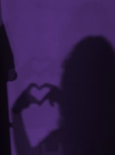 the shadow of a person standing in front of a purple wall holding a cell phone