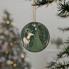 a christmas ornament hanging from a tree with a deer in the forest on it