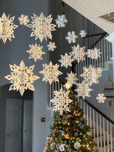 a christmas tree with snowflakes hanging from it's sides in front of a staircase