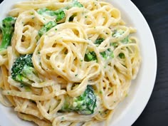 a white plate topped with pasta and broccoli on top of a black table