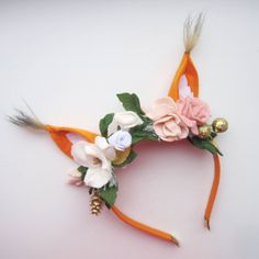 an orange headband with flowers and feathers on top of white surface, next to gold bells