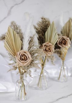 three vases with dried flowers in them on a marble counter top, one is filled with feathers and the other two are empty