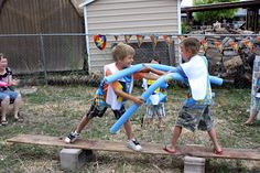 two young boys playing with inflatable toys on a wooden bench outside while others watch