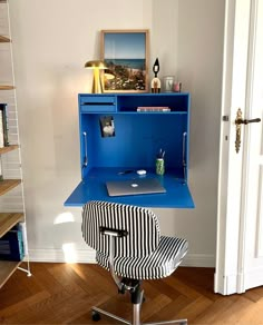 a blue desk with a black and white striped chair in front of it on a hard wood floor