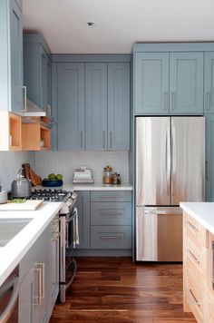 a kitchen with blue cabinets and white counter tops, wood flooring and stainless steel appliances