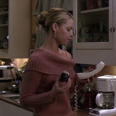 a woman standing in a kitchen holding a plate and looking at something on the counter