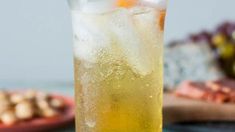 a tall glass filled with ice and lemonade on a table next to other food