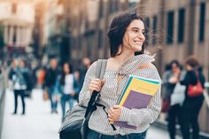 a woman is walking down the street with a book in her hand and holding a backpack