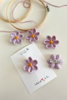 three crocheted flowers sitting on top of a white table next to a card