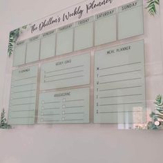 a wall mounted menu board on the side of a white wall with green plants and leaves