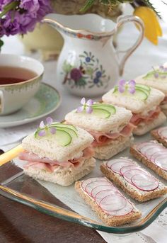 sandwiches with cucumber and ham are arranged on a plate next to a cup of tea