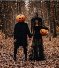 two people dressed up as witches holding hands in the woods with pumpkins on their heads