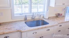 a kitchen sink sitting under a window next to a bowl of fruit on top of a counter