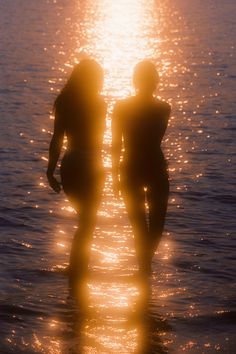 two people are standing in the water at sunset