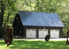 two garages in front of a black barn with three large sculptures on the lawn