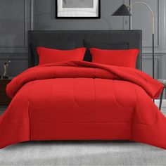 a bed with red sheets and pillows in a gray room next to a painting on the wall