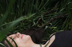 a woman laying down in the grass with her eyes closed and head tilted to the side