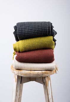 three blankets stacked on top of each other in different colors and sizes, sitting on a stool