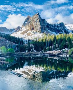 the mountains are covered in snow and trees near a lake with still water on it