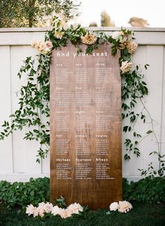 a wooden sign with flowers and greenery on it in front of a white fence