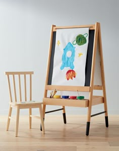 a child's art easel with a drawing on it and a wooden chair next to it