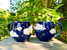 two blue mugs sitting on top of a wooden table in front of some trees