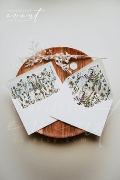 some cards are sitting on top of a wooden plate with leaves and flowers in them