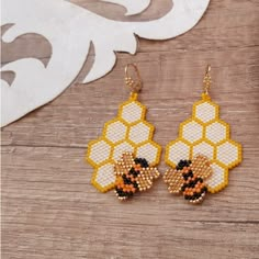 a pair of beaded bee earrings sitting on top of a wooden table