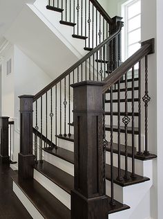 a staircase with black railing and wooden handrails in a white room next to a window