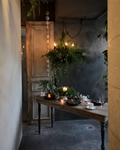 a wooden table topped with plates and cups next to a wall covered in greenery