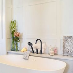 a white bath tub sitting next to a window with flowers in vases on it