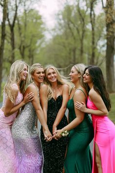 four beautiful young women standing next to each other in front of some trees and grass