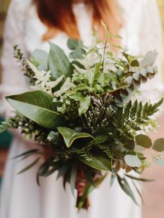 a woman holding a bouquet of flowers and greenery