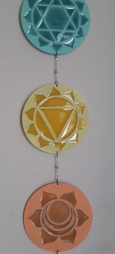 three metal ornaments hanging from the ceiling in front of a white wall with an orange, yellow and blue design on it