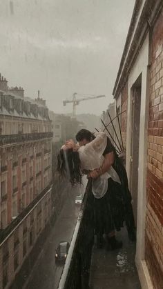 a man and woman kissing on the roof of a building in the rain with buildings behind them