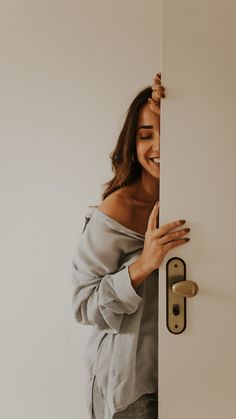 a woman peeking out from behind a door with her hand on the side of the door