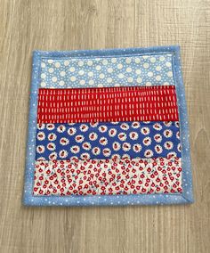 a red, white and blue patchwork quilt on a wooden surface with wood flooring