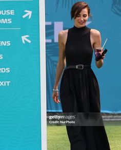 a woman in a black dress is standing next to a sign and holding a cell phone