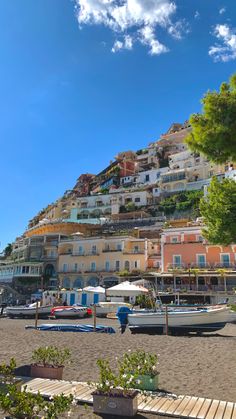 boats are parked on the beach in front of a hill with many houses and trees