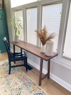 a wooden table sitting next to a window with blinds on the windowsill and a chair in front of it