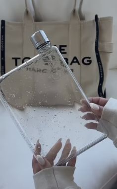 a woman is holding a clear bottle in front of her face and hand with water on it