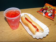 a hot dog with ketchup next to a drink