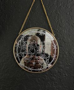 a circular mirror hanging on a wall with gold chains and an image of two people