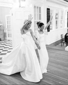 two women in white dresses standing on a wooden floor with their hands up to the sky