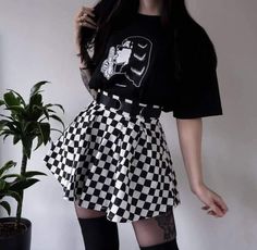 a woman in black and white checkered skirt with thigh high socks standing next to a potted plant